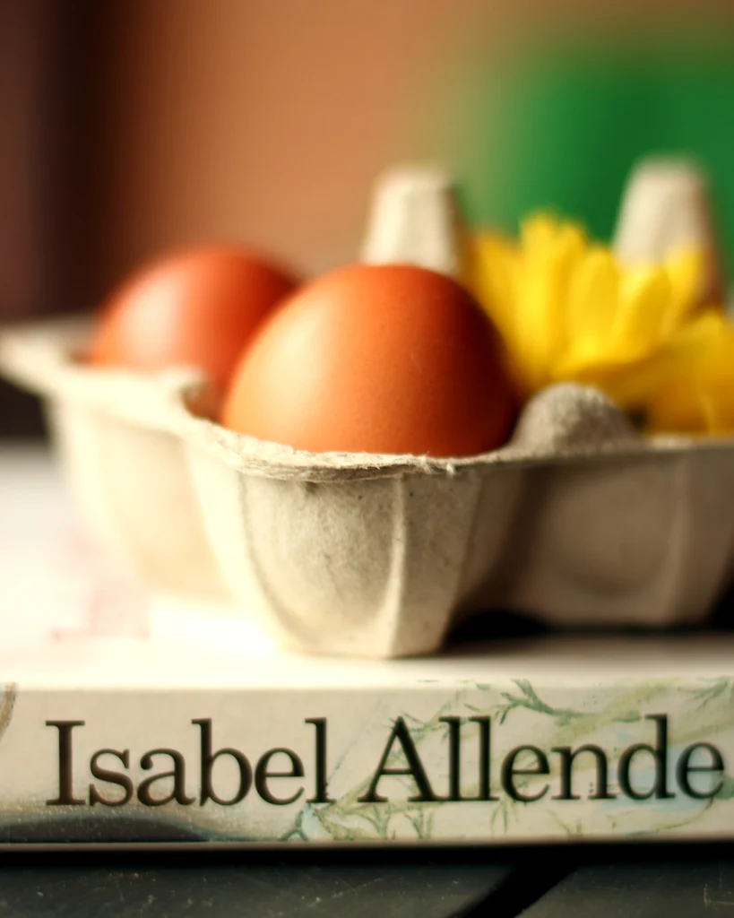 Cartone di uova visto di lato, poggiato sul libro Afrodita di Isabel Allende, di cui si vede il dorso con la stampa del nome dell'autrice