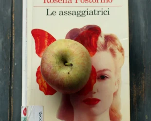 La copertina del libro Le assaggiatrici, di Rosella Postorino, raffigura il viso di una donna bionda parzialmente coperto dalla stampa in rosso di una farfalla. Al centro di questa farfalla ho poggiato una mela fuji. L'ho scelta come simbolo di integrità per parlare di etica e scrittura