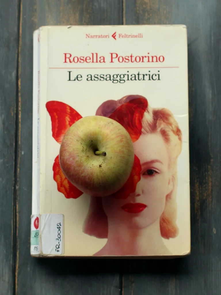 La copertina del libro Le assaggiatrici, di Rosella Postorino, raffigura il viso di una donna bionda parzialmente coperto dalla stampa in rosso di una farfalla. Al centro di questa farfalla ho poggiato una mela fuji. L'ho scelta come simbolo di integrità per parlare di etica e scrittura